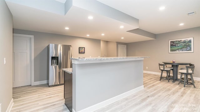 kitchen with stainless steel fridge, light stone countertops, a kitchen island, and light hardwood / wood-style flooring