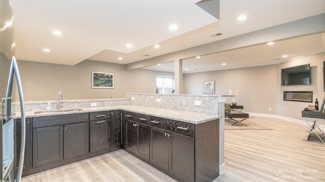 kitchen with light stone counters, sink, stainless steel refrigerator, and light wood-type flooring