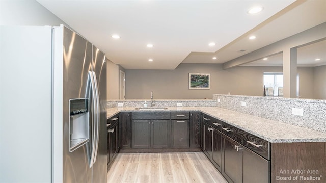 kitchen with sink, stainless steel fridge, kitchen peninsula, light stone countertops, and light hardwood / wood-style flooring