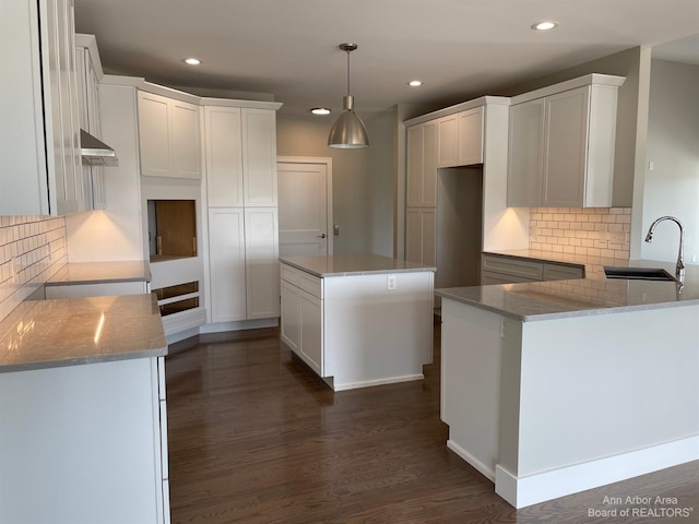 kitchen with light stone counters, sink, a kitchen island, and white cabinets