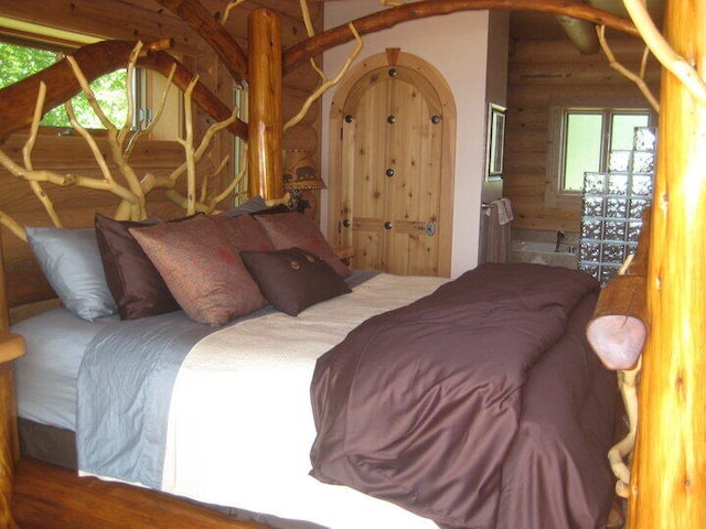 bedroom with wood finished floors, log walls, and vaulted ceiling