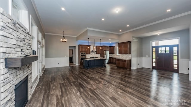 living room featuring dark wood-type flooring, ornamental molding, a stone fireplace, and a chandelier