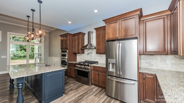 kitchen featuring sink, appliances with stainless steel finishes, hanging light fixtures, a center island with sink, and wall chimney exhaust hood