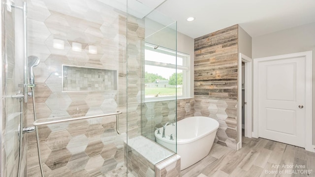 bathroom with independent shower and bath, hardwood / wood-style floors, and tile walls