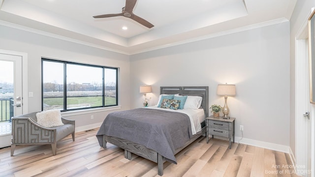 bedroom with ceiling fan, a tray ceiling, and light hardwood / wood-style floors