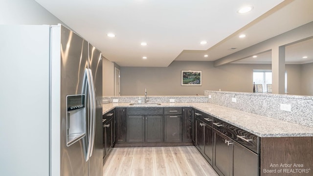 kitchen with sink, light hardwood / wood-style floors, kitchen peninsula, stainless steel refrigerator with ice dispenser, and light stone countertops