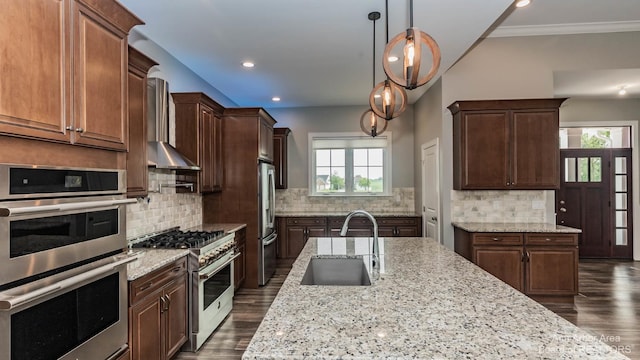 kitchen with wall chimney exhaust hood, sink, light stone counters, hanging light fixtures, and stainless steel appliances