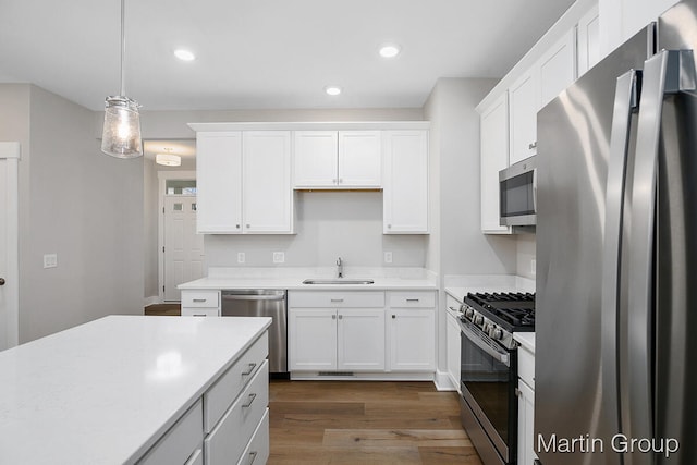 kitchen with dark hardwood / wood-style floors, pendant lighting, sink, stainless steel appliances, and white cabinetry