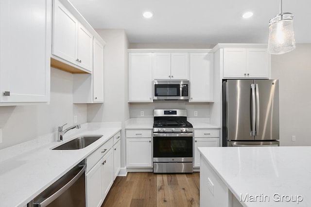 kitchen with sink, hanging light fixtures, appliances with stainless steel finishes, wood-type flooring, and white cabinetry