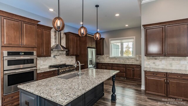 kitchen featuring appliances with stainless steel finishes, decorative light fixtures, an island with sink, sink, and light stone counters