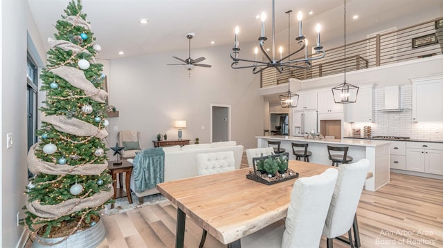 dining room with ceiling fan, a towering ceiling, and light wood-type flooring