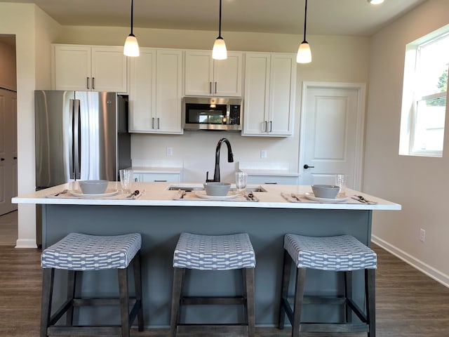 kitchen featuring stainless steel appliances, a kitchen island with sink, pendant lighting, and white cabinets