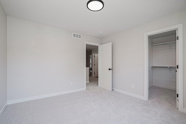 unfurnished bedroom with a walk in closet, light colored carpet, and a closet