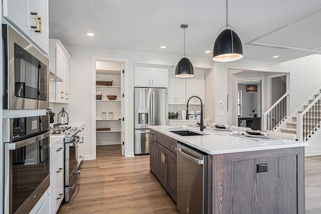 kitchen featuring stainless steel appliances, an island with sink, sink, and white cabinets