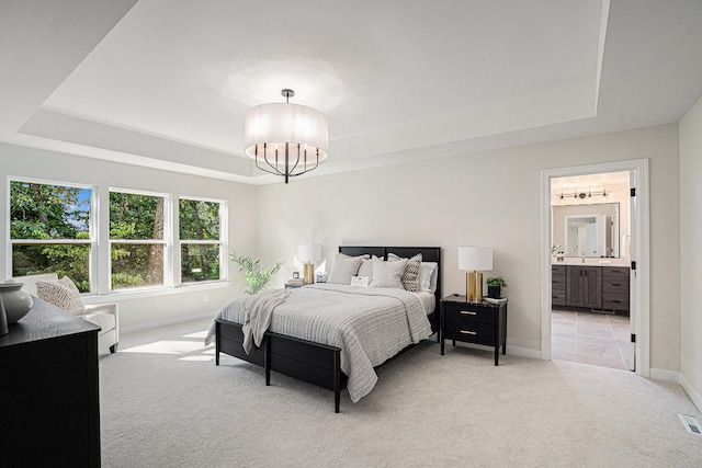 carpeted bedroom with ensuite bathroom, a tray ceiling, and a notable chandelier