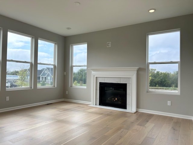 unfurnished living room featuring plenty of natural light, light wood-type flooring, and a tiled fireplace