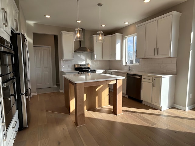 kitchen with appliances with stainless steel finishes, wall chimney exhaust hood, white cabinets, a kitchen island, and hanging light fixtures