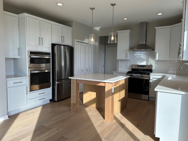 kitchen featuring wall chimney exhaust hood, stainless steel appliances, sink, white cabinets, and a kitchen island