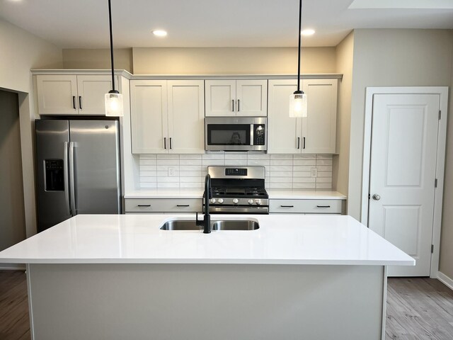 kitchen featuring backsplash, stainless steel appliances, a center island with sink, light hardwood / wood-style floors, and hanging light fixtures