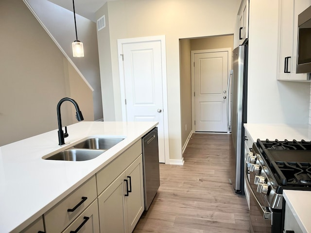 kitchen with sink, light hardwood / wood-style flooring, hanging light fixtures, and appliances with stainless steel finishes