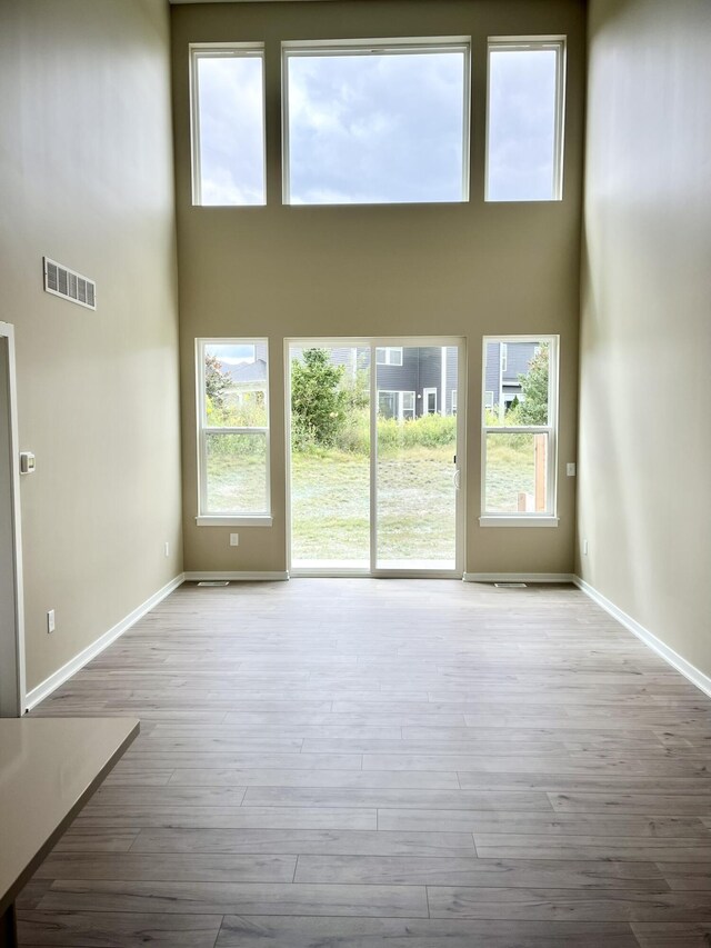 unfurnished living room featuring a towering ceiling and light hardwood / wood-style floors