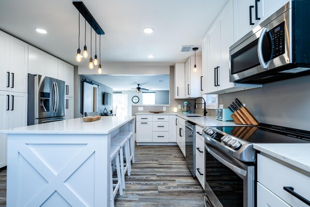 kitchen with white cabinets, appliances with stainless steel finishes, a kitchen island, and dark hardwood / wood-style floors