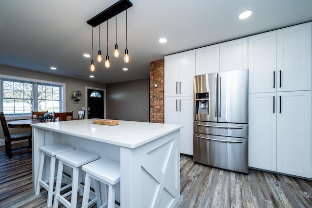 kitchen with light stone countertops, stainless steel refrigerator with ice dispenser, hardwood / wood-style floors, a center island, and white cabinetry