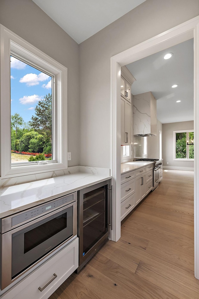 kitchen featuring white cabinetry, wall chimney range hood, and wine cooler