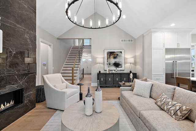 living room with light hardwood / wood-style flooring, a notable chandelier, vaulted ceiling, and a premium fireplace