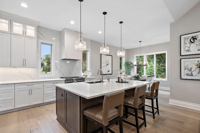 kitchen featuring tasteful backsplash, premium range hood, a center island with sink, and white cabinets