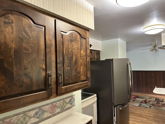 kitchen with wood walls, dark brown cabinets, stainless steel refrigerator, electric stove, and light hardwood / wood-style floors