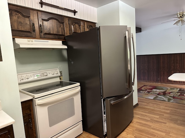 kitchen featuring stainless steel fridge, wooden walls, dark brown cabinetry, white electric stove, and light wood-type flooring