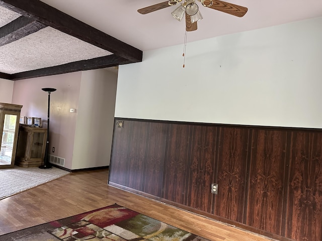 empty room with hardwood / wood-style flooring, ceiling fan, and beam ceiling