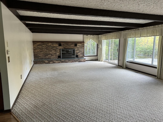 unfurnished living room with beamed ceiling, plenty of natural light, carpet floors, and a fireplace