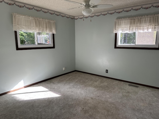 carpeted empty room with ceiling fan, plenty of natural light, and a textured ceiling