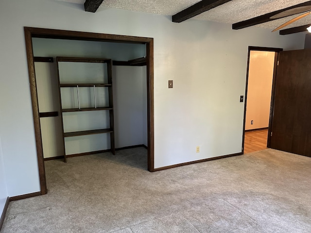 carpeted empty room with ceiling fan, beam ceiling, and a textured ceiling