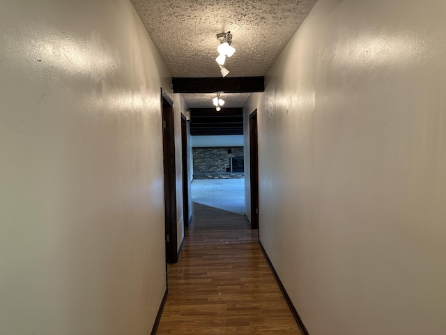 hallway with dark hardwood / wood-style flooring, beam ceiling, and a textured ceiling