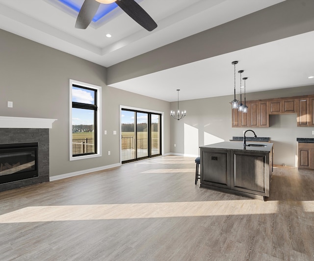 kitchen with ceiling fan with notable chandelier, a kitchen island with sink, sink, light hardwood / wood-style floors, and a stone fireplace