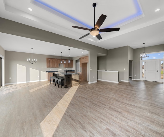 unfurnished living room featuring a raised ceiling, hardwood / wood-style floors, ceiling fan with notable chandelier, and sink