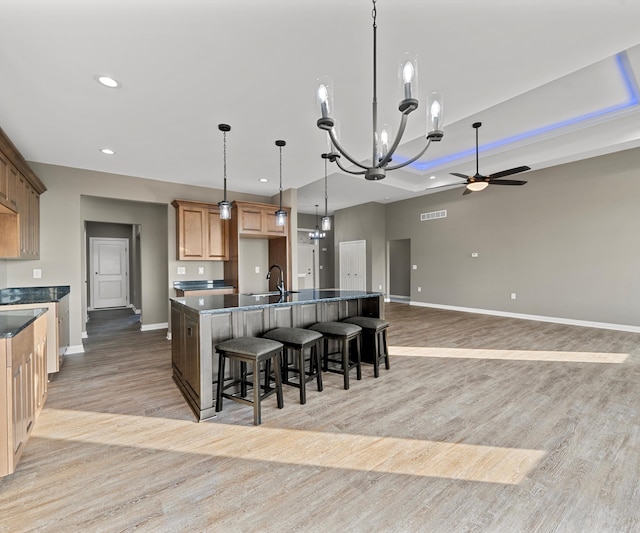 kitchen featuring pendant lighting, ceiling fan with notable chandelier, light wood-type flooring, a large island, and a breakfast bar area