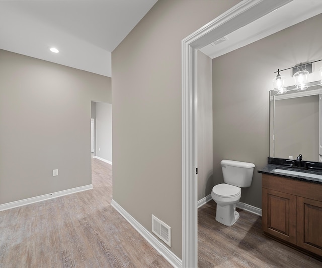 bathroom with toilet, wood finished floors, vanity, visible vents, and baseboards