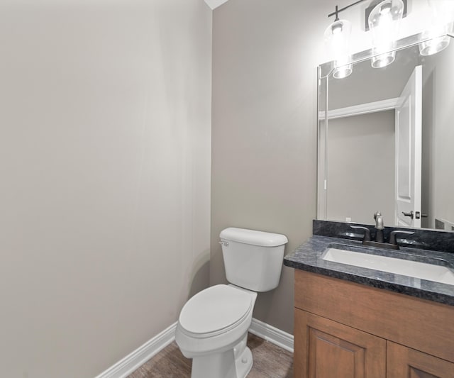 half bathroom featuring baseboards, vanity, toilet, and wood finished floors