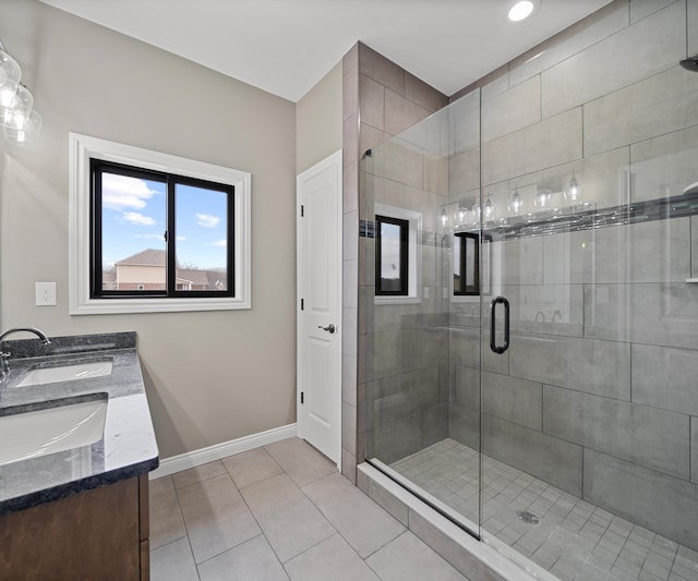 bathroom featuring a sink, baseboards, tile patterned floors, double vanity, and a stall shower