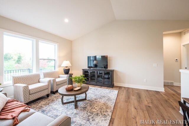 living room with a wealth of natural light, light hardwood / wood-style flooring, and lofted ceiling