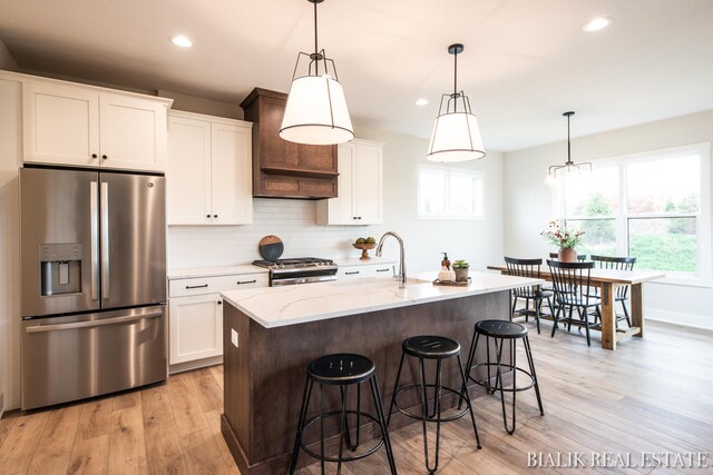 kitchen featuring light wood-type flooring, appliances with stainless steel finishes, decorative backsplash, light stone counters, and white cabinets