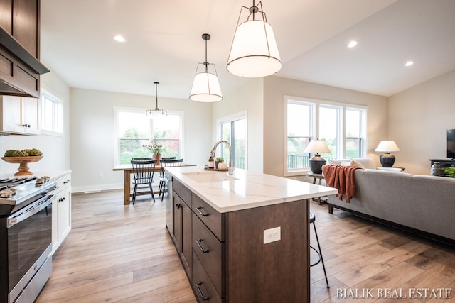 kitchen with sink, stainless steel stove, light hardwood / wood-style flooring, and an island with sink