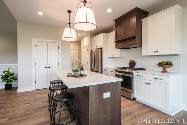 kitchen featuring light wood-type flooring, backsplash, hanging light fixtures, an island with sink, and appliances with stainless steel finishes