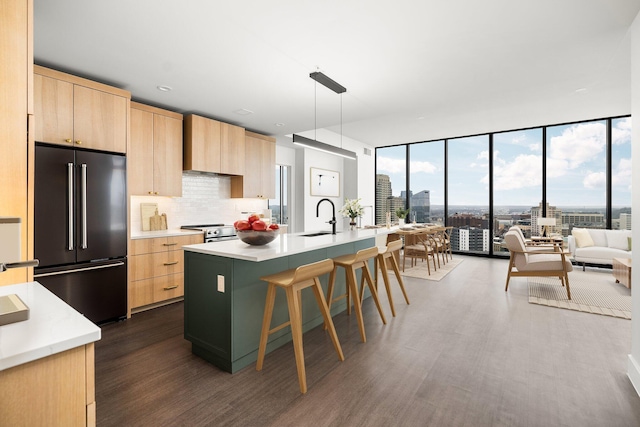 kitchen with appliances with stainless steel finishes, light brown cabinetry, tasteful backsplash, decorative light fixtures, and an island with sink