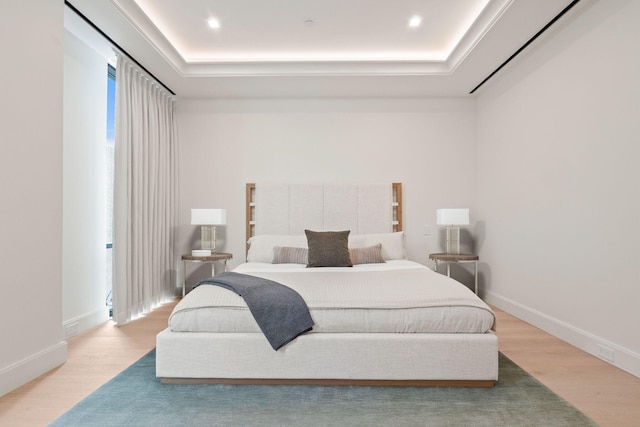 bedroom with baseboards, a raised ceiling, and wood finished floors