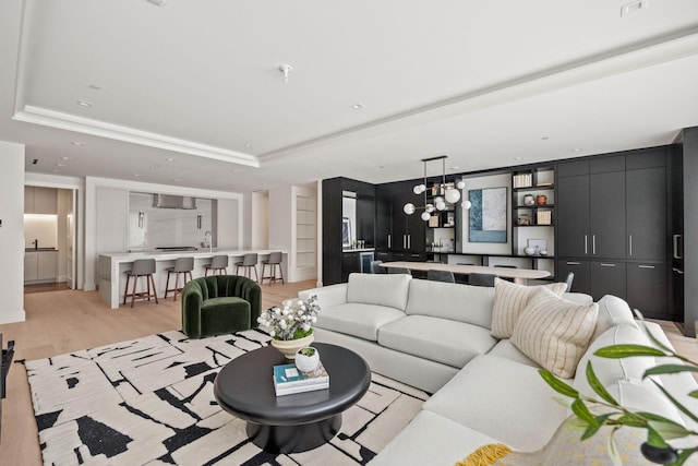 living room featuring sink, light wood-type flooring, an inviting chandelier, and a tray ceiling